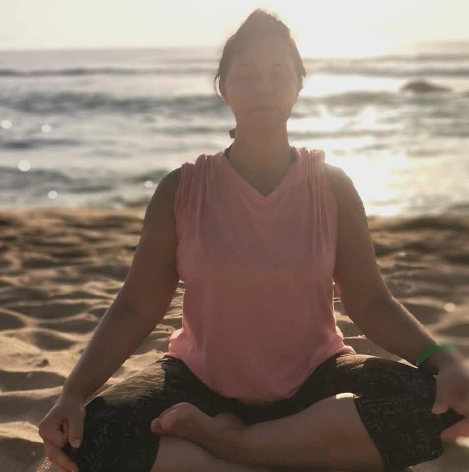 Yoga and meditation instructor, sitting in lotus pose on a sandy beach